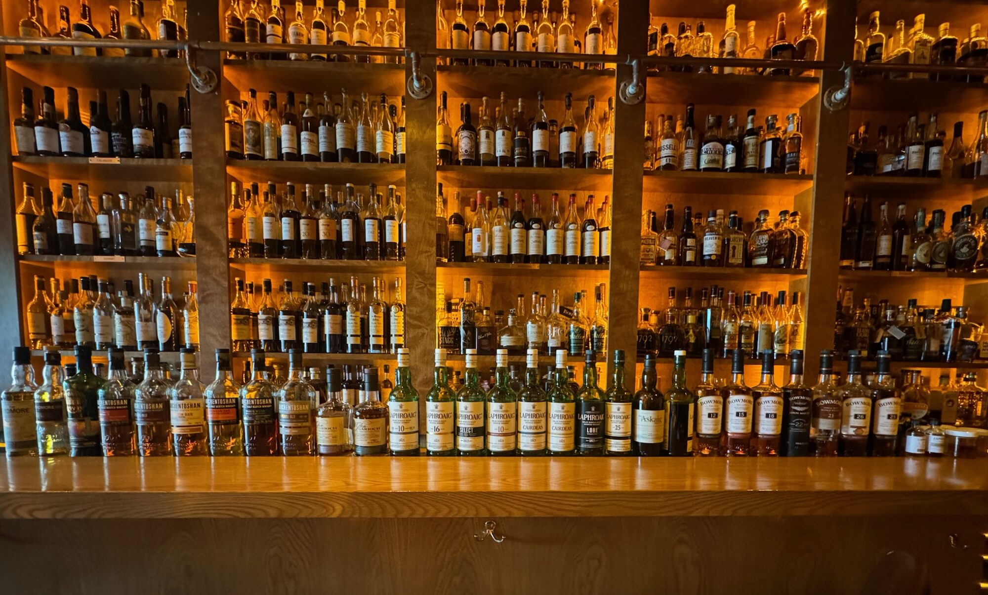 Multiple whiskies laid out in a row on the bar with the whisky shelves in the background